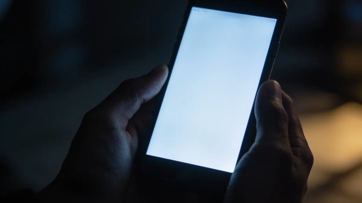 Leuchtendes Smartphone in dunklen Händen – Symbolbild digitale Erpressung